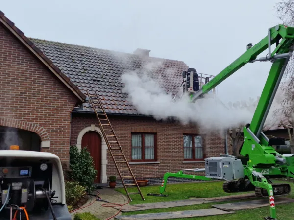 Hoogwerker en ladder bij een bakstenen woning terwijl het pannendak ontmost wordt