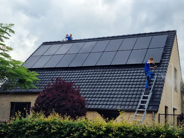 Medewerker op het dak van een woning met zonnepanelen, ladder tegen de gevel